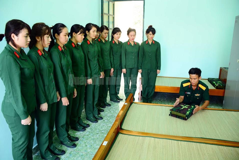 Cán bộ trung đội hướng dẫn nữ chiến sĩ gấp chăn màn.