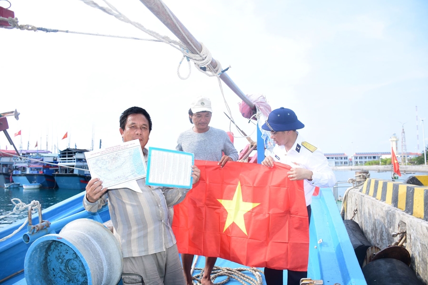 Cán bộ Trung tâm Dịch vụ hậu cần-kỹ thuật đảo Trường Sa trao cờ Tổ quốc tặng ngư dân và phát tờ rơi tuyên truyền khi tàu cá vào neo đậu tại âu tàu. 