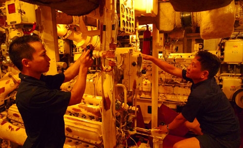 Máy trưởng, Thượng úy Trần Xuân Ly (phải) và Thiếu úy Lưu Đức Hải đang kiểm tra máy móc trong khoang máy, “buồng phổi” của con tàu, duy trì hoạt động thường xuyên trong điều kiện khó khăn trên biển. Nhiệt độ trung bình trong khoang máy luôn ở mức 45 độ C.