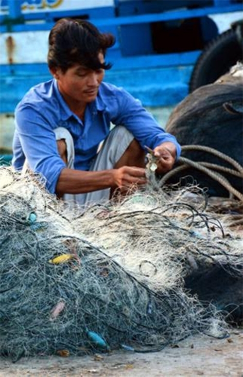 Bên cầu tàu, một ngư dân đang gỡ tấm lưới chuẩn bị cho chuyến ra khơi.