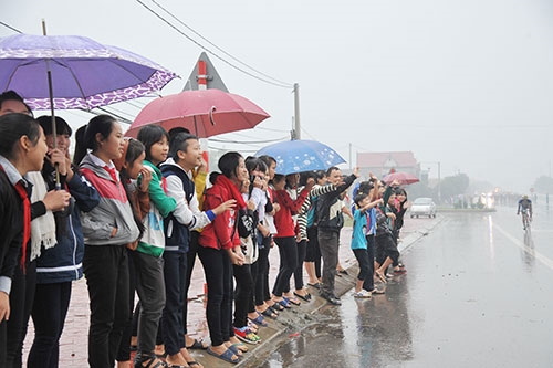 Nhiều em học sinh đứng bên đường cầm ô cổ vũ đoàn đua.